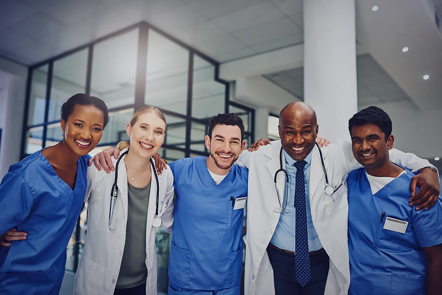 A diverse clinical team standing together, arms around each other